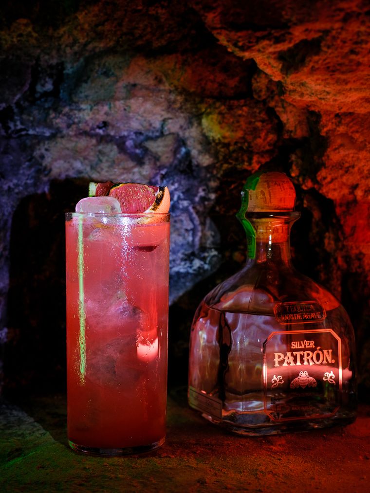 Cócteles rojos iluminados con luz de color junto a la botella de tequila