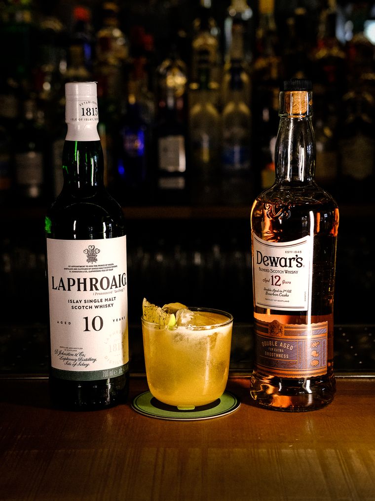 Whisky Sour con espuma junto a las botellas de whisky